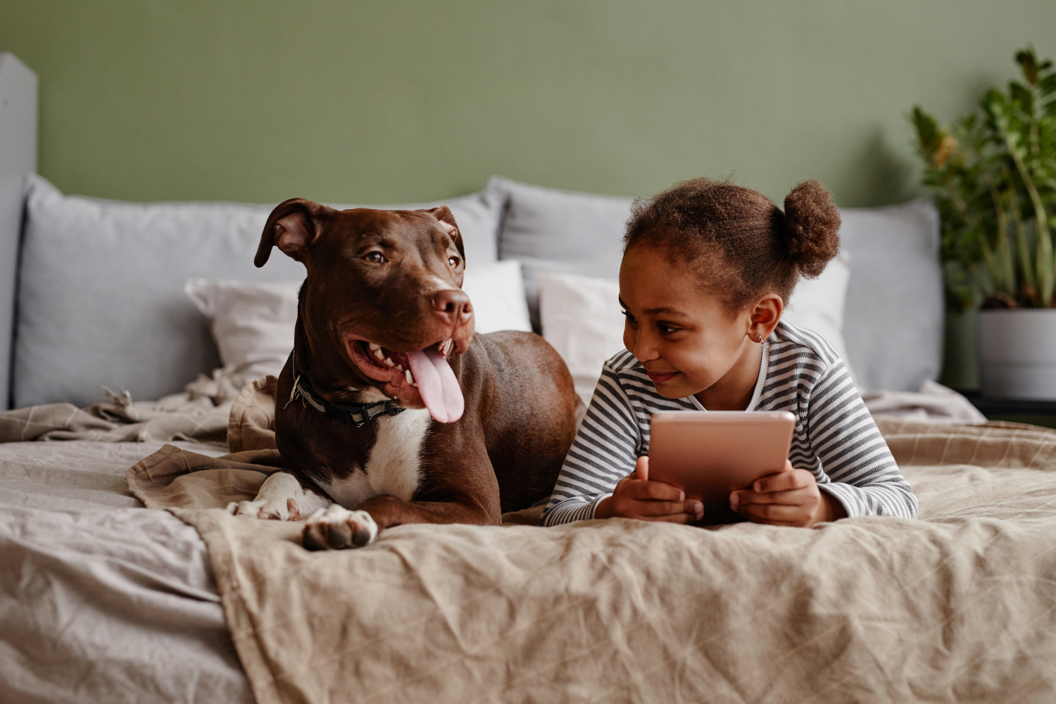 young girl laying next to a brown dog on a bed